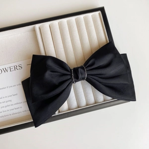 Detail of elegant black satin bow hair clip with sparkling rhinestone center and vintage style