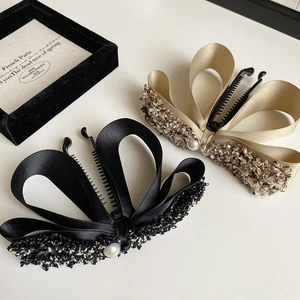 Detail of satin bow hair clips with tweed trim and pearl accent in black and gold