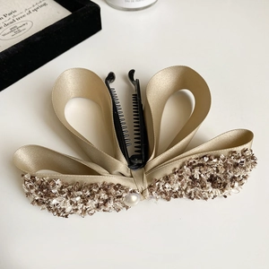 Detail of a champagne satin bow hair clip with tweed borders and a pearl center