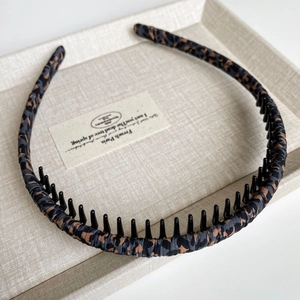 Detail of leopard print fabric headband with non-slip inner teeth on a beige tray