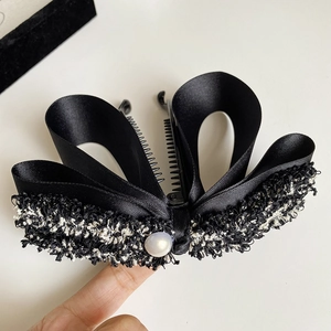 Detail of banana hair clip featuring black satin ribbon and tweed fabric with faux pearl