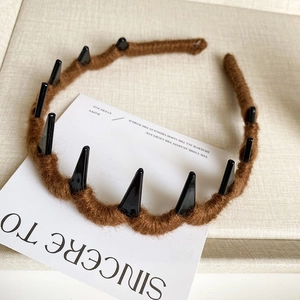 Close-up of brown plush headband with black spiked design and wave comb teeth detail