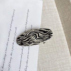 Detailed view of the zebra pattern oval hair clip on a decorative paper background