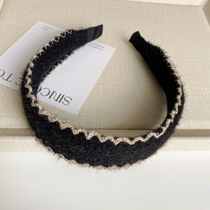 Détail du serre-tête en peluche noire avec bordure dorée tressée sur plateau beige