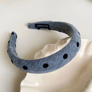 Detail view of handmade grey polka dot headband with woven label on a ceramic plate