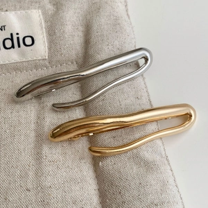 Detailed view of wave-shaped gold and silver metal hair clips on a linen pouch