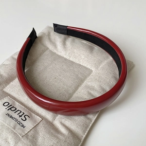 Close-up of a glossy red leather headband with a black inner lining on linen
