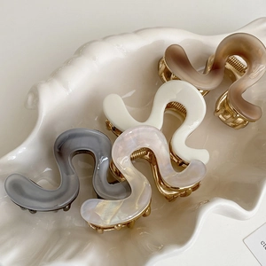 Elegant wavy acetate shark hair clips in marble and neutral tones on a ceramic tray