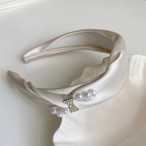 Close-up of champagne satin headband with rhinestone butterfly and white pearls decoration
