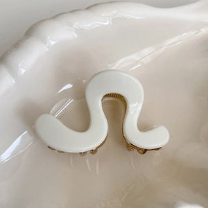 Close-up of elegant cream acetate hair claw clip with golden metal spring and wave design
