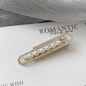 Détail de la pince à cheveux trombone dorée avec diamants et perles blanches