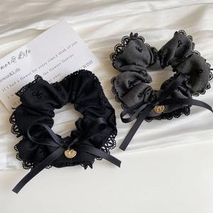 Close-up of grey and black lace hair scrunchies with ribbon bows and gold heart pendants