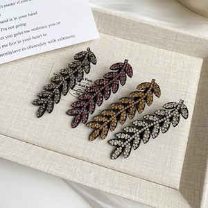 Detailed close-up of leaf-shaped hair clips with sparkling rhinestones in four elegant colors