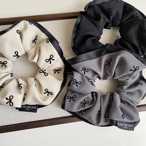 Detailed view of three fabric bow-patterned scrunchies in white, gray, and black colors