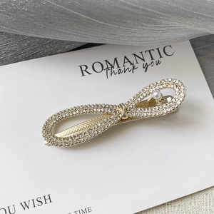 Détail d'une barrette à cheveux dorée en forme de nœud avec strass et perle blanche