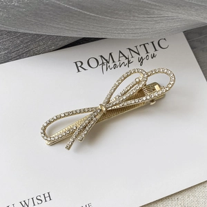 Détail d'une barrette noeud dorée ornée de strass brillants sur une carte blanche chic