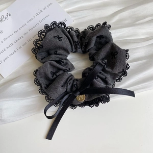 Detail of dark grey scrunchie featuring black lace trim and embroidered bow patterns