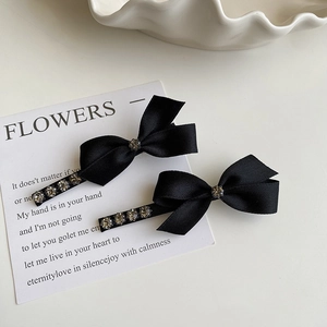 Paio di fermagli per capelli con fiocco nero e strass su elegante carta bianca
