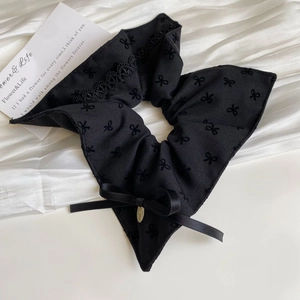 Close-up of black fabric hair scrunchie with lace trim and elegant bow embroidery detail