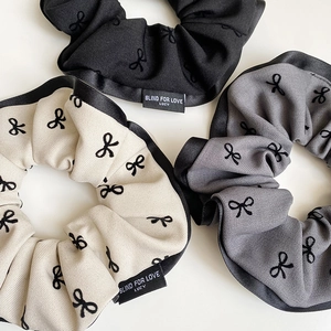 Detail of fabric scrunchies in beige, grey, and black with bow embroidery and text labels