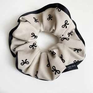 Detail of beige scrunchie with black bow prints and silk satin piping finish