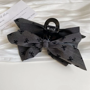 Detail of dark grey bow hair claw clip with black pattern on elegant white satin