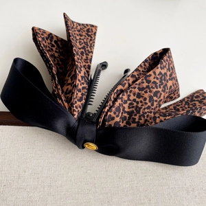 Vue détaillée de la grande pince à cheveux satinée avec nœud léopard et logo Wings doré