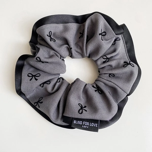 Detail of grey ribbed fabric scrunchie with bow prints and BLIND FOR LOVE label