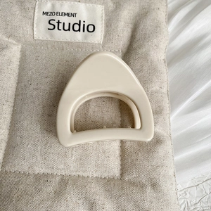 Détail d'une pince à cheveux géométrique beige mat sur un fond en tissu texturé