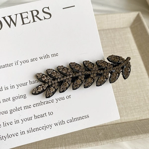 Close-up of a sparkling leaf-shaped wheat rhinestone hair clip on a vintage card