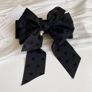 Detail view of a large black ribbon bow hair clip with an elegant pearl pendant