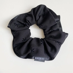 Close-up of black scrunchie with bow patterns and Blind For Love text label