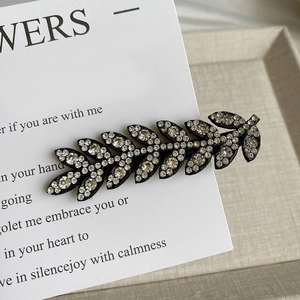 Macro detail of leaf-shaped sparkling hair clip with white crystals on a black base