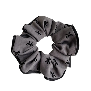 Grey fabric scrunchie with black bow prints and ribbon edges on a white background