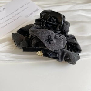 Detail of grey tweed hair claw with black bow embroidery and a golden butterfly charm