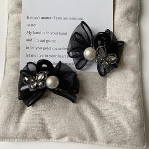 Detailed close-up of a black mesh bow hair clip with white pearl and rhinestone butterfly decor
