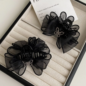 Détail de pinces à cheveux à nœud en maille noire avec papillon en strass dans une boîte