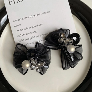 Detailed macro view of two black mesh bow hair clips with silver rhinestones and pearls