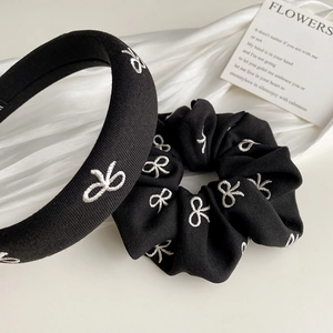 Détail de la texture du serre-tête et chouchou noirs avec broderies de nœuds blancs