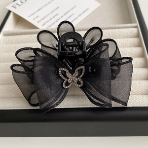 Détail d'une pince à cheveux avec nœud en maille noire et strass brillants dorés