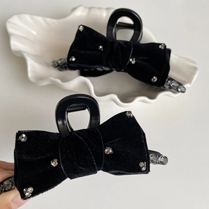 Elegant black velvet bow hair claw clip with rhinestones shown on a white ceramic plate