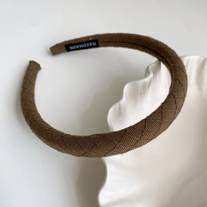 Detail of brown quilted fabric headband with handmade label on white display plate