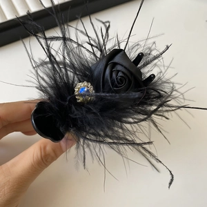 Close-up of black feather hair claw with silk rose and a blue heart rhinestone accent