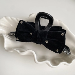 Elegant black velvet bow hair claw clip with rhinestones on a white ceramic jewelry plate