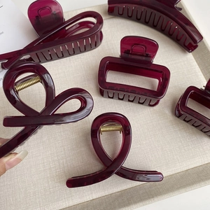 Dettagli di mollette per capelli bordeaux in resina con molle dorate su vassoio beige