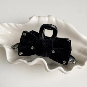 Close-up of black velvet bow hair claw clip with rhinestones on a white shell tray