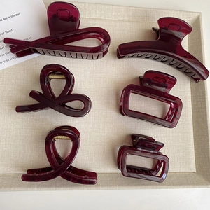 Dettaglio di sei mollette per capelli bordeaux in varie forme su un vassoio da esposizione