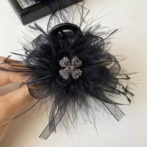 Detailed shot of black feather hair claw with mesh bow and clover rhinestone jewelry