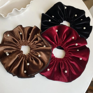 Close-up of three velvet scrunchies with white pearls in black, burgundy and brown colors