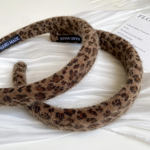 Close-up of leopard print faux fur headband with hand made woven label on silk background